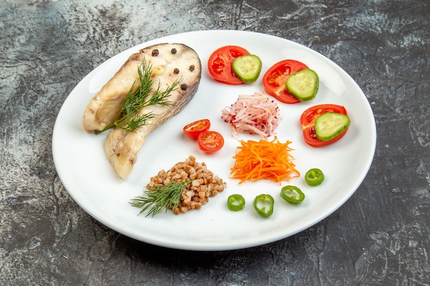 Close up view of boiled fish buckwheat served with vegetables green on a white plate on ice surface with free space