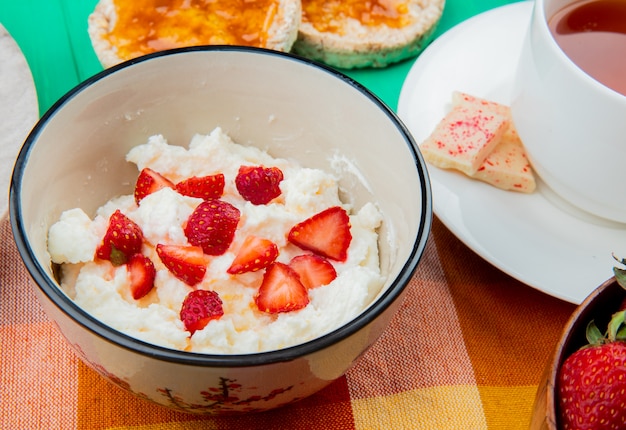 Close-up view of bowl of cottage cheese with strawberries cup of tea crispbreads on cloth