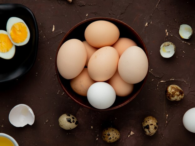 Close-up view of bowl of eggs with other eggs around on maroon background