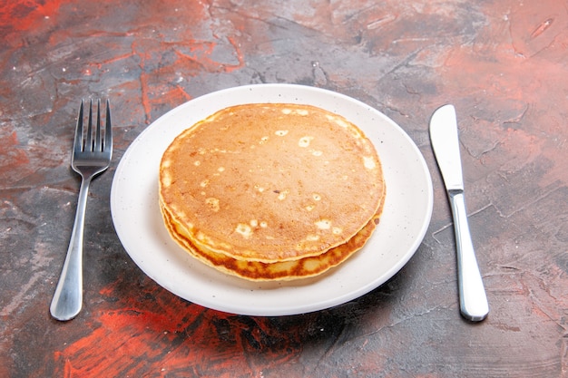 Close up view of buttermilk pancakes on a white plate and knife with fork on mixed color