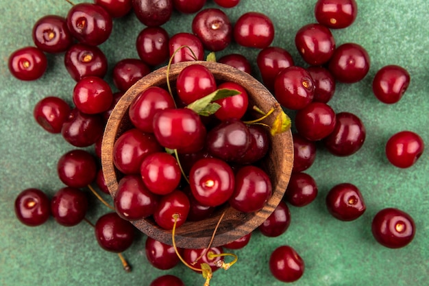 Close-up view of cherries in wooden bowl and on green background