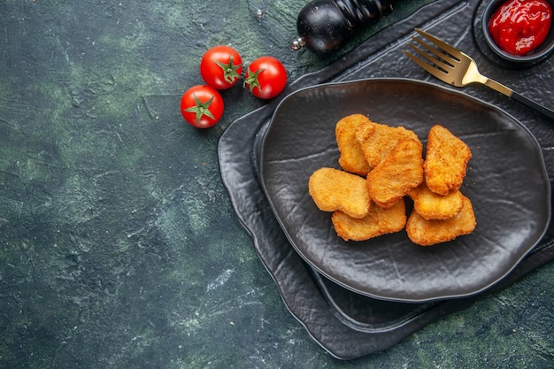 Close up view of chicken nuggets on a black plate and elegant fork ketchup on dark color tray white flower tomatoes on the left side