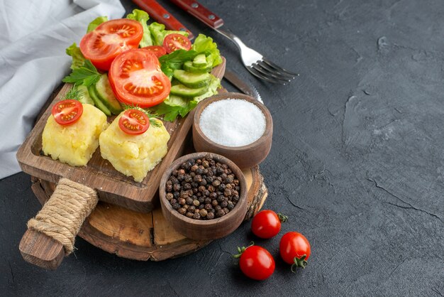 Close up view of chopped and whole fresh vegetables cheese on cutting board and spices cutlery set on black surface