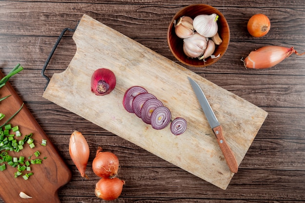 Close-up view of cut red onion on cutting board with garlic shallot and knife on wooden background