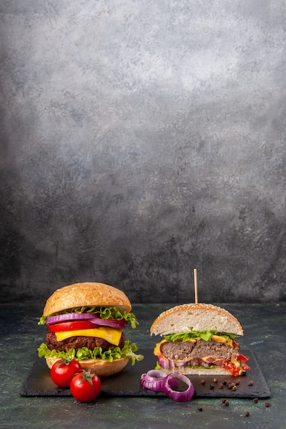 Close up view of cut whole tasty sandwiches and tomatoes with stem onions on black tray on dark mix color surface