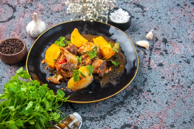 Free Photo close up view of delicious dinner with meat potatoes served with green in a black plate and garlic spices fallen oil bottle flower on mix colors background