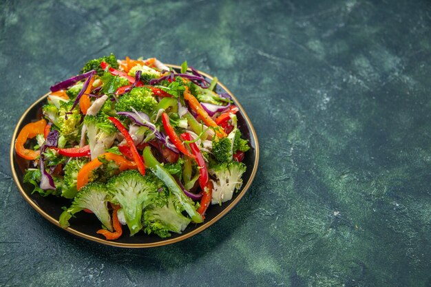 Close up view of delicious vegan salad in a plate with various fresh vegetables on the right side on dark background