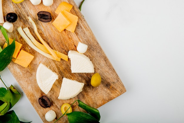 Free photo close-up view of different kinds of cheese with grape pieces olives on cutting board on white decorated with flowers and leaves with copy space