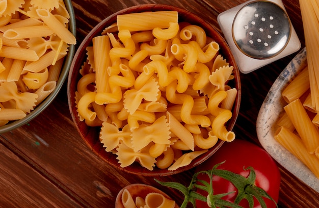 Free Photo close-up view of different types of macaroni in bowls and salt tomato on wooden surface