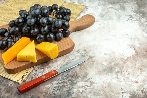 Free Photo close up view of fresh delicious black grape bunch and various kinds of cheese on wooden cutting board and knife on mixed color background