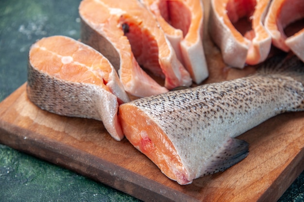 Close up view of fresh raw fishes on brown wooden cutting board on dark mix colors table with free space