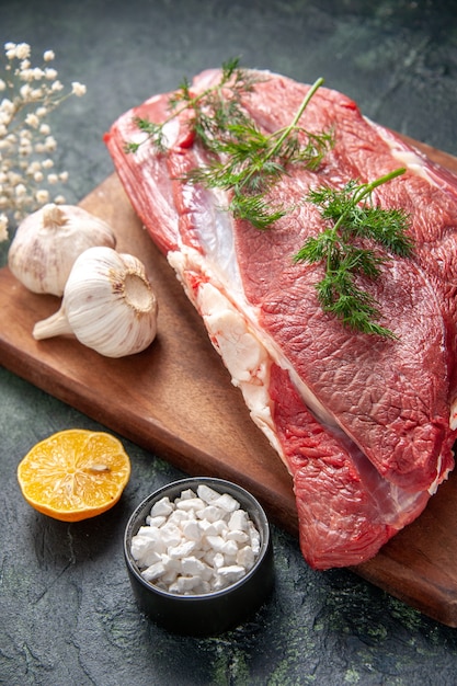 Close up view of fresh raw red meats green garlics knife on brown wooden cutting board salt lemon flower on dark color background