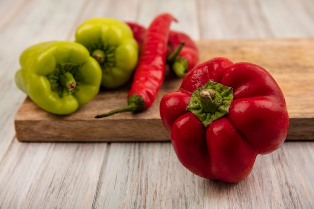 Close up view of a fresh red bell pepper with colorful bell and chili peppers on a wooden kitchen board on a grey wooden background