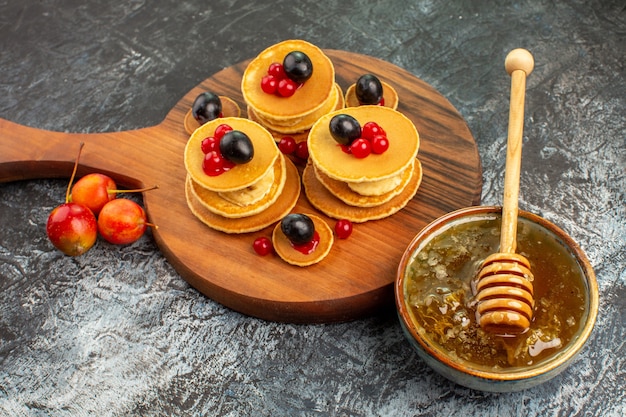 Close up view of fruit pancakes on wooden cutting board honey in a white bowl on gray