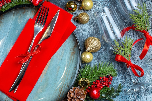 Close up view of glass goblets with red ribbon cutlery set on a blue plate and fir branches decoration accessories on dark background