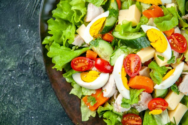 Close up view of homemade delicious salad in a black plate on the left side on green black mix colors background with free space