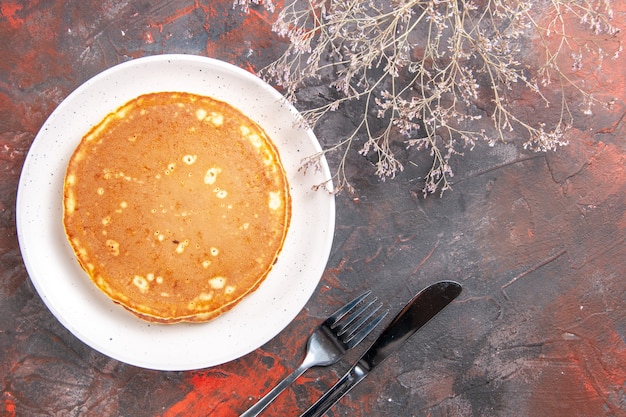 Close up view of homemade pancakes on a white plate and knife with fork on mixed color