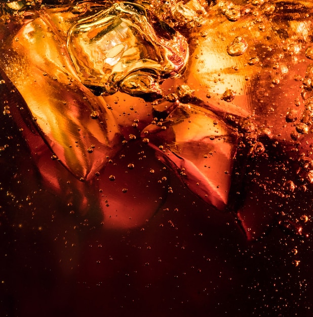 Close up view of the ice cubes in dark cola background. Texture of cooling sweet summer's drink with foam and macro bubbles on the glass wall. Fizzing or floating up to top of surface.