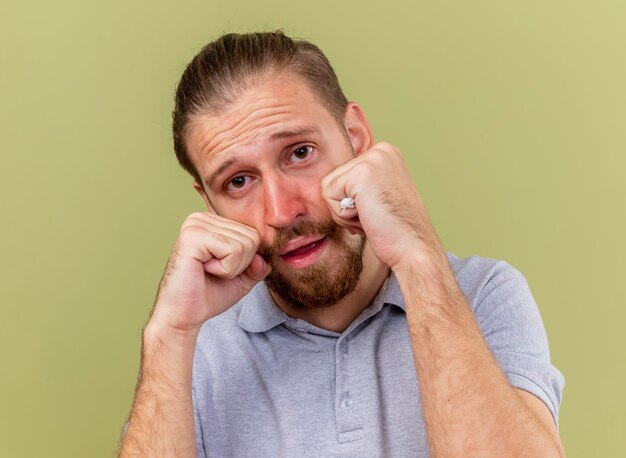 Close-up view of impressed young handsome slavic ill man hoding napkin keeping fists on face  isolated on olive green wall