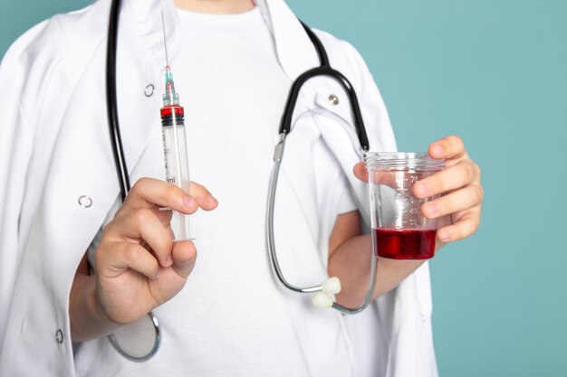 close up, view little child boy cute adorable sweet holding injection and red liquid in white medical suit on blue wall