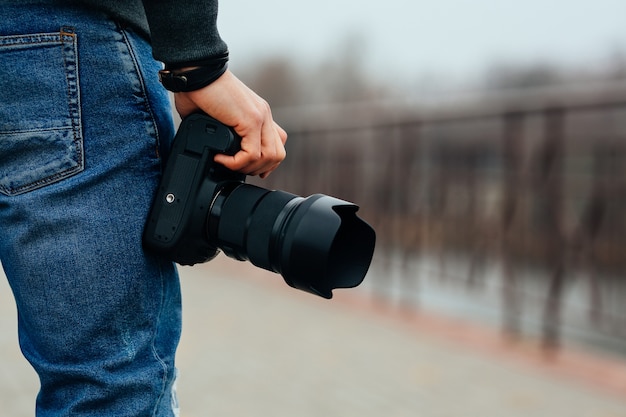 Close-up view of male hand holding professional camera on the street.