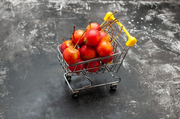 Close up view of mini shopping chart with red cherries on gray