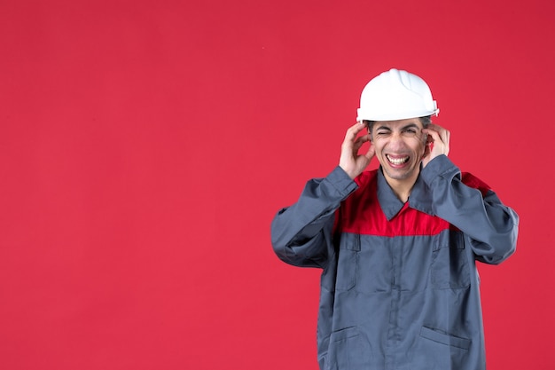 Free photo close up view of nervous young architect in uniform with hard hat on isolated red wall