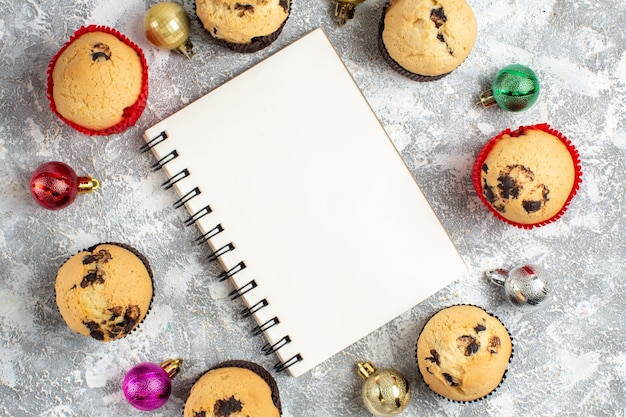 Close up view of notebook among freshly baked delicious small cupcakes and decoration accessories on ice table