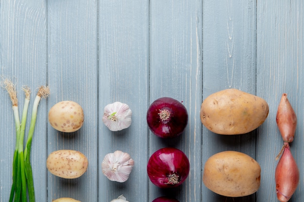 Free photo close up view of pattern of vegetables as scallion potato garlic onion on wooden background with copy space