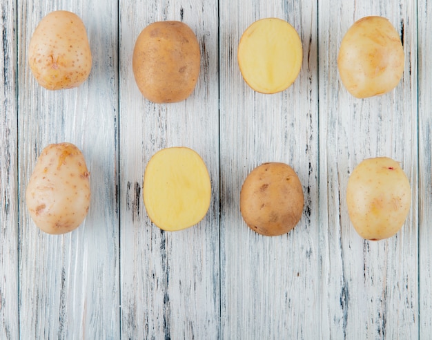 Free photo close up view of pattern of whole and cut potatoes on wooden background with copy space