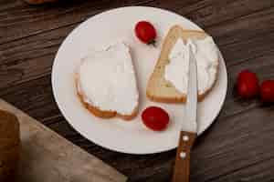 Free photo close-up view of plate of white bread slices smeared with cottage cheese and tomatoes and knife on wooden background