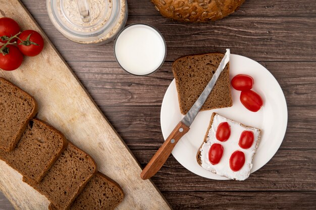 Close-up view of plate with rye bread slices and tomatoes and knife with milk oat-flakes on wooden background