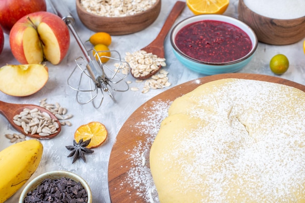 Close up view of raw pastry flour on round board grater fresh fruits jam cookies chocolates on stained white background