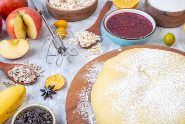 Close up view of raw pastry flour on round board grater fresh fruits jam cookies chocolates on stained white background