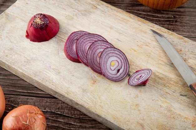 Close-up view of sliced red onion with knife on wooden surface and wooden background