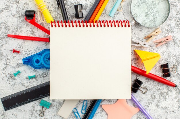 Close up view of spiral closed spiral notebook and various office appliances on white surface