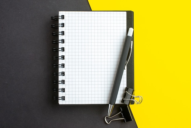 Close up view of spiral notebook on book and pens on black yellow background with free space