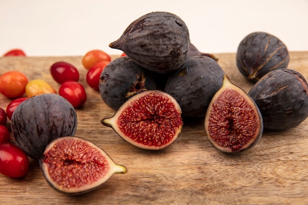 Close up view of sweet black figs on a wooden kitchen board with cornelian cherries isolated on a white wall