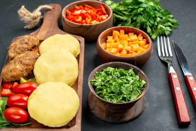 Close up view of tasty cutlets with vegetables with fork and knife on dark