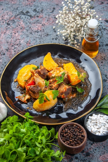 Free photo close up view of tasty dinner with meat potatoes served with green in a black plate and spices garlic oil bottle