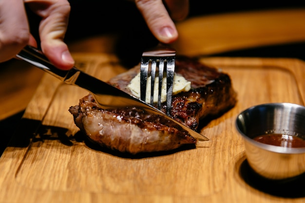 Free Photo close-up view of tasty steak with sauce. male's hands begin to cut a slice.