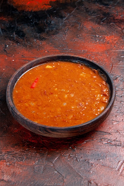 Close up view of tomato soup in a brown bowl on mixed color table