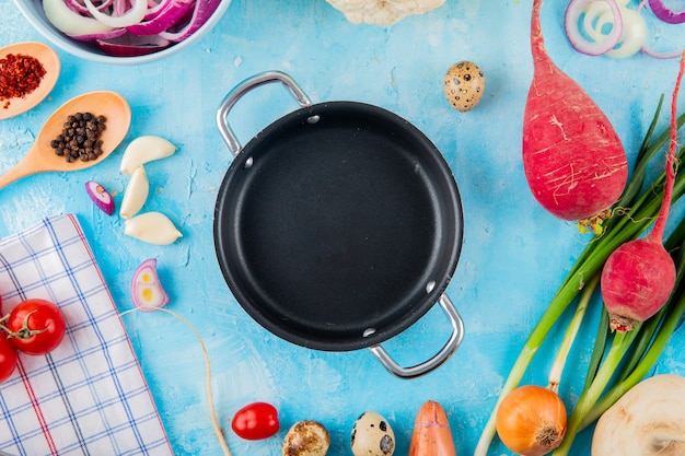 Free Photo close-up view of vegetables as garlic onion radish with spices and braiser pan on center on blue background