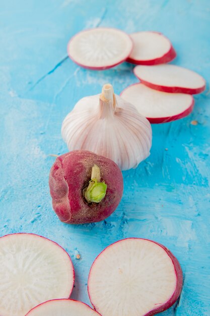 Close-up view of vegetables as sliced and whole radish and garlic on blue background