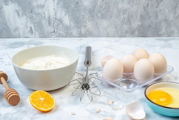 Close up view of white flour in a bowl and stainless cooking tool eggs lemon slice on two-toned background