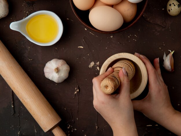 Close-up view of woman hands pressing garlic in garlic-crusher with butter eggs rolling pin