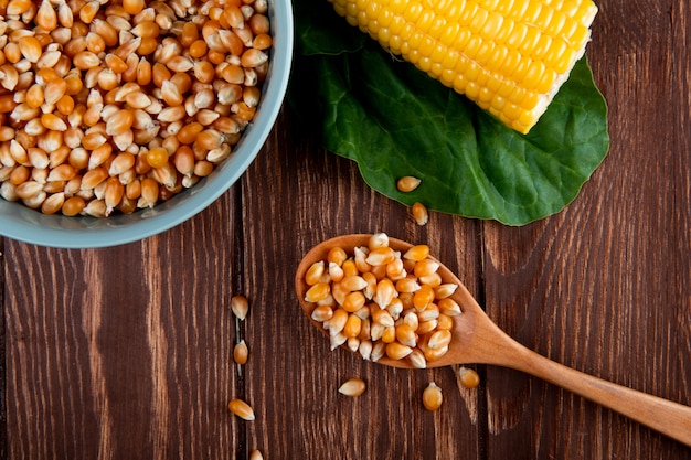 Close-up view of wooden spoon full of dried corn seeds with cooked corn and spinach on wooden surface