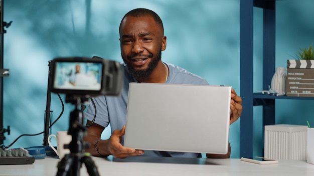 Close up of vlogger reviewing modern laptop on camera with tripod. Social media influencer using device to review product and give recommendation for vlog channel. Blogger recording video