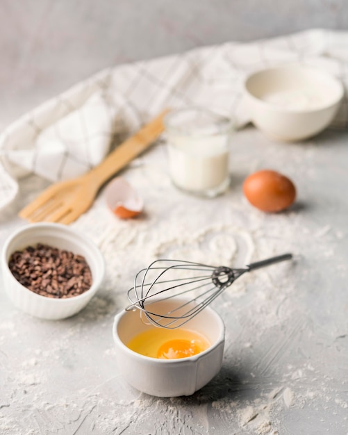 Close-up whisk with egg and baking flour on the table