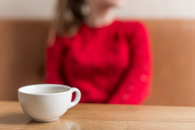 Close-up of white cup with blurred woman background